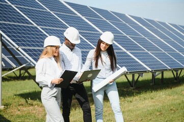 Group of multi ethnic people and safety helmets staring at solar farm.