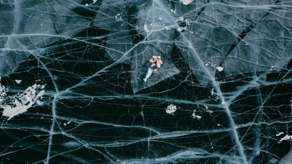 A tourist girl in bright clothes and sunglasses smiles happily, lies on the frozen blue ice of Lake Baikal and controls the drone up. An incredible pattern of crack bubbles. Siberia Russia tourist