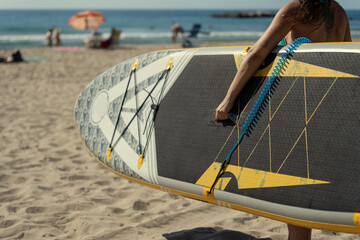 Woman carrying paddle board walking on the beach
