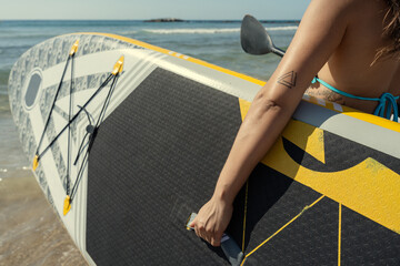 Woman holding paddle board getting ready for stand up paddling on the beach