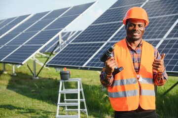 African american man in safety helmet on solar panels with screwdriver. Competent technician using tools while performing service work on station