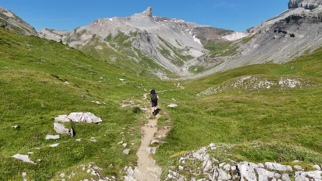 Male hiker (man) with trekking backpack hiking on path towards mountain panorama with summit Tita Seri in Swiss Alps, Switzerland