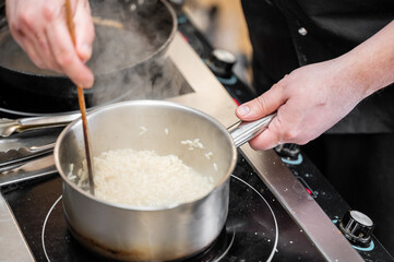 A chef stirs risotto in a stainless steel pot on a stovetop, with steam rising as the dish cooks, showcasing a professional cooking process and culinary artistry.