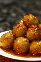 Cilok is a traditional food from Indonesia, made from tapioca, round shape, chewy textured. White plate on the gray gravel. Selective focus