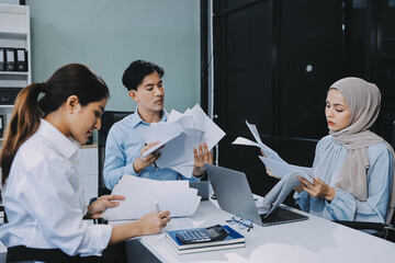 Fototapeta premium Young asian businesswoman suffering from headache while colleagues arguing and blaming her for bad work results during stressful office meeting
