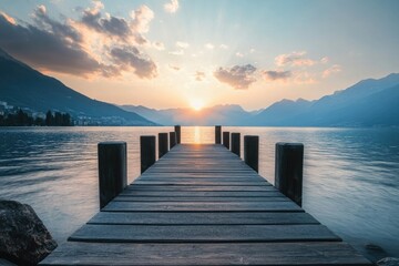 Fototapeta premium A serene wooden pier extends into a tranquil lake at sunset, framed by majestic mountains and soft clouds, symbolizing peace, reflection, and the beauty of nature