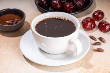 Healthy organic date seed coffee, black coffee cup, made with grated date seeds, with whole date fruits and seeds on beige background . Alternative coffee hot drink