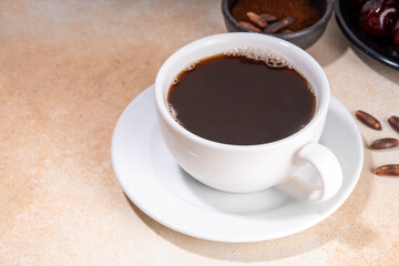 Healthy organic date seed coffee, black coffee cup, made with grated date seeds, with whole date fruits and seeds on beige background . Alternative coffee hot drink