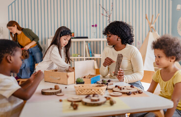 Preschool teacher guides a diverse group of children in a natural materials activity in a bright,...