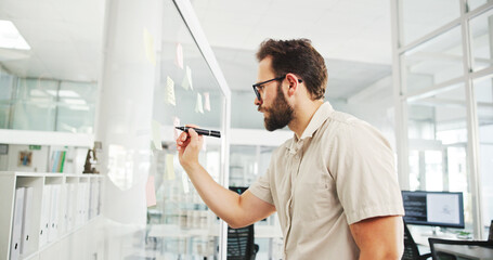 Fototapeta premium Business, glass wall and man in office, writing and decision with brainstorming for proposal. Person, employee and sales consultant in workplace, problem solving and planning for project or choice