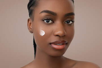 Glowing skin and a touch of cream define this beauty skincare portrait of a young African American woman with braided hair and natural makeup.