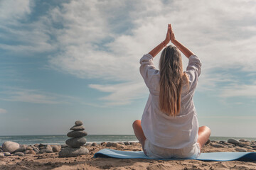 Woman meditating on beach with stack of zen stones during summertime