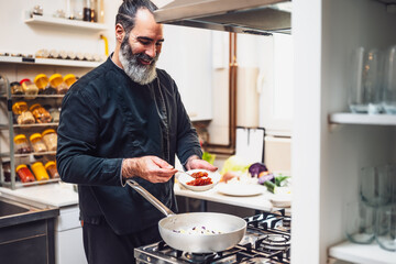 Professional chef is preparing meal in restaurant's kitchen. He makes a vegetarian lunch. He is adding spices.