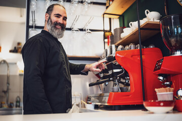 Professional barista in black apron working in restaurant. Portrait of happy barmen who is making coffee in his bar.