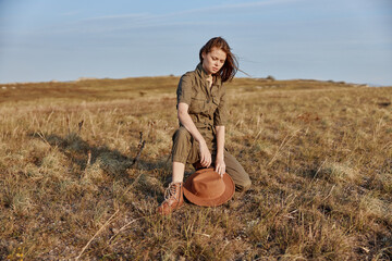 Woman sitting in a field with a hat in hand, exploring nature and enjoying relaxing vacation time