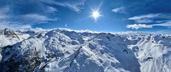 A breathtaking aerial view of a beautiful winter landscape with snow-covered alpine mountains, sunny skies, and scenic slopes perfect for skiing, snowboarding, hiking, and outdoor adventures