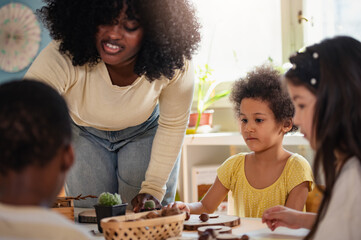 Preschool teacher guides a diverse group of children in a natural materials activity, encouraging creativity, sensory play, and inclusive early childhood learning through hands-on exploration.
