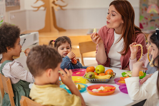 Happy preschool children of diverse backgrounds enjoying a healthy snack with their teacher in a bright and cheerful classroom setting