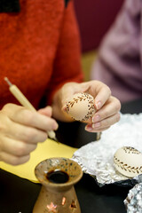 Woman hands painting Easter eggs with black bee wax, traditional Lithuanian method