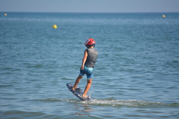 Young boy practicing hydrofoiling on the calm waters of a beach during a sunny day
