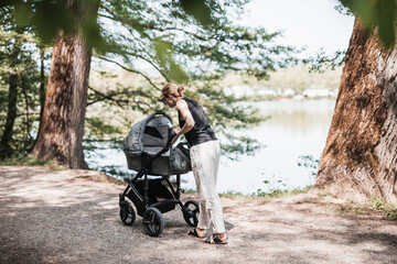 Rear view of casually dressed mother walking with baby stroller in Koseski bajer city park in Ljubljana, Slovenia. Family, child and parenthood concept.