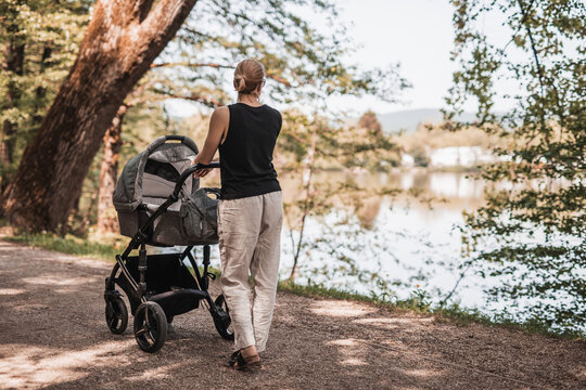 Rear view of casually dressed mother walking with baby stroller in Koseski bajer city park in Ljubljana, Slovenia. Family, child and parenthood concept.