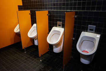 Modern public restroom with orange walls and white ceramic urinals separated by partitions