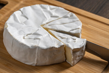 Cutting of white soft moldy Camembert cheese on a wooden cutting board with knife , closeup