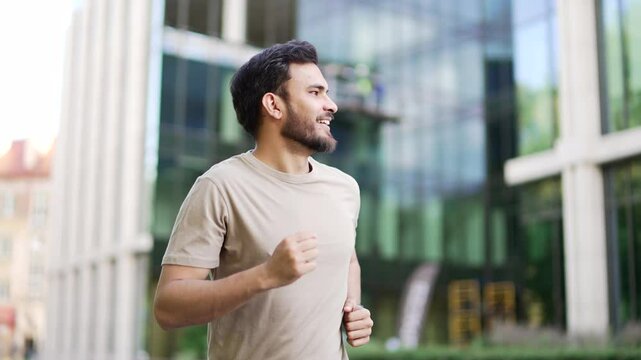 Young adult male runner jogging along a park alley on a city street. Handsome active man in a t-shirt enjoys jogging outdoors. Athlete on morning workout. Sport and healthy lifestyle concept. Close up