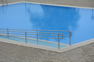 Poolside view with a smooth blue surface and metallic railing at a modern facility during daytime