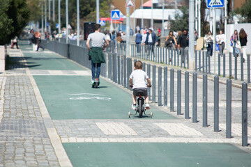 Children and adults enjoying a sunny day riding scooters and bikes on a busy urban pathway