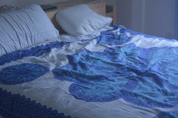Cozy bedroom featuring a blue patterned bedspread with disheveled bedding in soft morning light