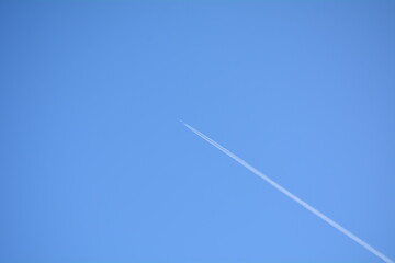Clear blue sky with a high-flying airplane leaving a contrail during midday