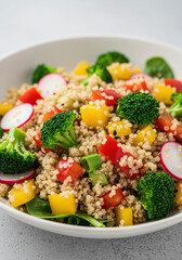 A colorful quinoa salad with fresh vegetables in a white bowl on a gray surface