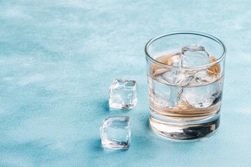 Glass with ice cubes on cold surface under blue lighting showing clear transparency of water and melting process with condensation droplets forming visible edges