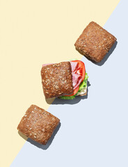 Fresh sandwich with ham, lettuce, tomato, and sauce on whole grain bread on a yellow blue background.