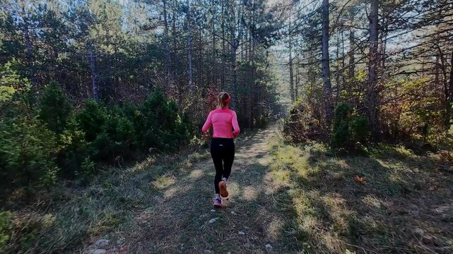 Candid shot of a female trail runner jogging through an autumn forest in the mountains. Morning outdoor workout showcases active lifestyle, fitness, endurance, and nature-focused marathon training
