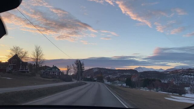 Early morning drive through Northern Norway. Snowy mountains and empty roads bathed in soft orange sunlight at dawn. Peaceful rural scenery in Troms region.