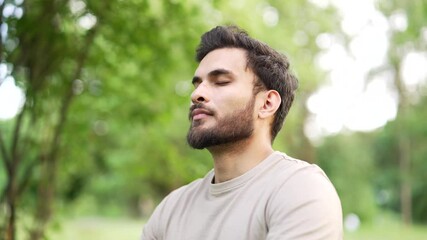 Happy sports man meditating deep breathing sitting in urban city park. Adult handsome male practices yoga outside. Smiling athlete feels relieved, relaxes with eyes closed enjoying nature. Close up