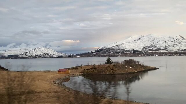Early morning drive through Northern Norway. Snowy mountains and empty roads bathed in soft orange sunlight at dawn. Peaceful rural scenery in Troms region.
