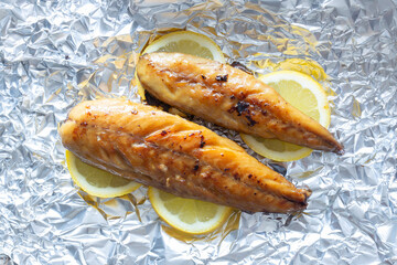 Smoked mackerel fillets cooked with sliced lemon on an aluminium background backdrop.