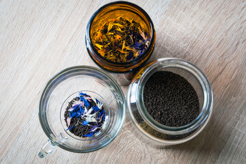 Dried cornflowers in glass, transparent cup used for tea. Edible flowers of Centaurea with intense blue, rose and white pigment. Organic tea idea. Granulated black tea mixed with cornflowers petals. 