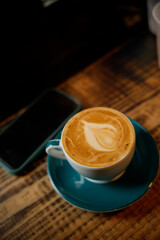 Cappuccino with latte art and smartphone resting on rustic wooden table