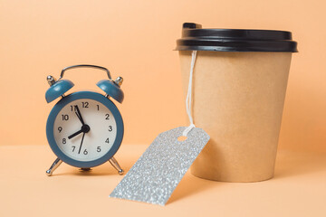 Blue alarm clock sits on a table next to a coffee cup with a silver tag on it