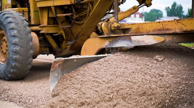 Low angle close-up of motorized grader spreading gravel to level road base on highway construction site