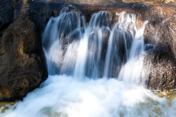Obraz premium Long exposure of a small waterfall cascading over rocks with soft focus. Smooth water texture evokes a peaceful summer scene in nature. Perfect for wellness and backgrounds.