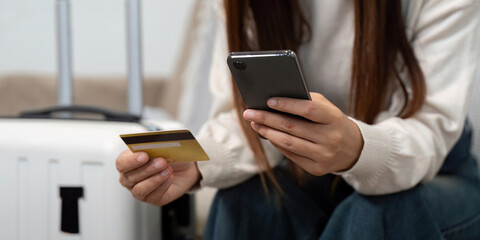Travel Planning and Digital Convenience. A woman checks travel details using her smartphone and credit card.