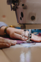 woman sews piece of cloth on sewing machine. industrial metal machine for all fabric tops. female seamstresses work in clothing workshop. industrial equipment - sewing machines. professional tailors. 