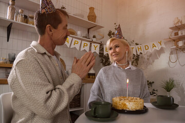 Senior couple celebrating birthday with cake and tea in kitchen