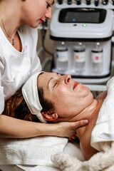 Satisfied mature adult woman receiving professional face and neck massage in beauty spa or salon. Modern cosmetics and beauty concept.